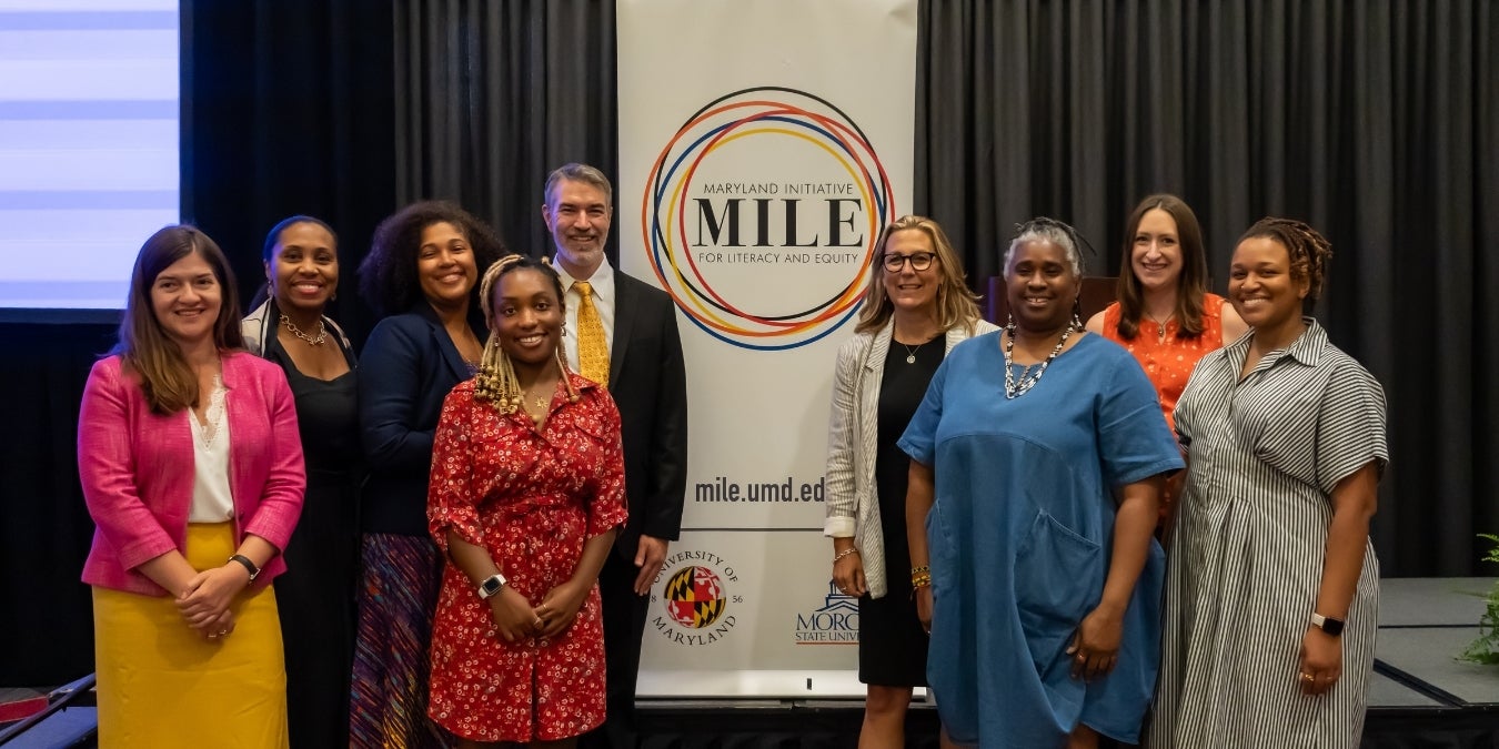 MILE faculty stand in front of a sign with the MILE logo
