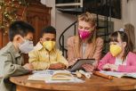 Children and teacher with masks looking at tablet