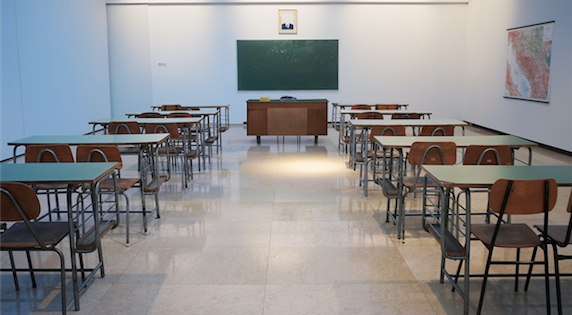 Empty classroom with a blank chalkboard and chairs and desks